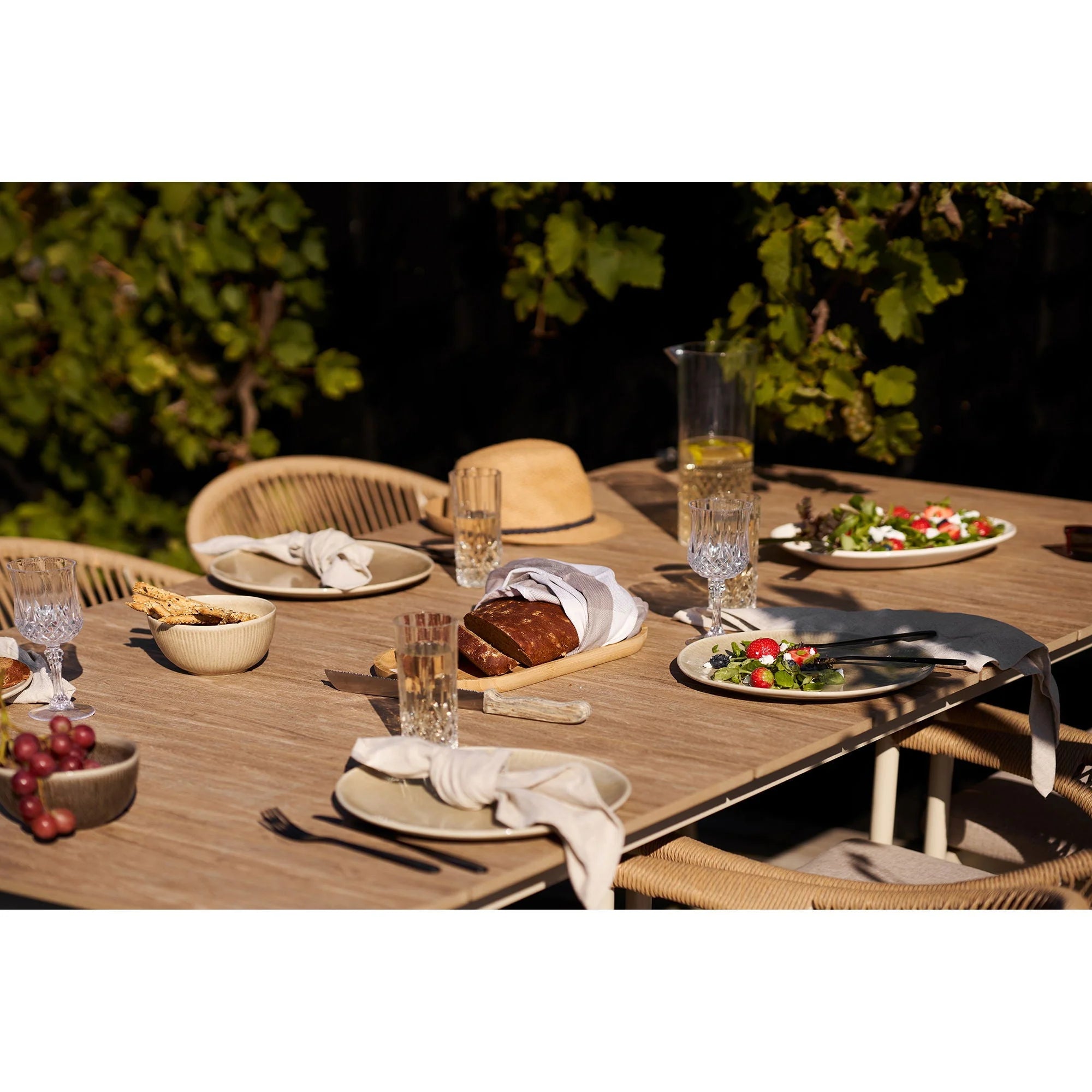 Table en bois d’extérieur avec chaises en rotin tressé et chapeau de paille