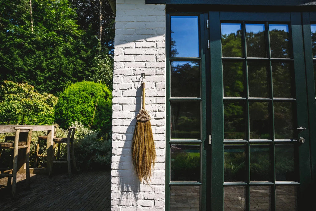 Balai mural décoratif en raphia naturel à franges H75 cm contre mur blanc