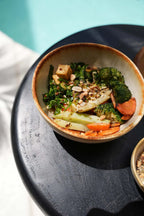 Bol en céramique artisanale beige avec légumes rôtis, tofu et noix