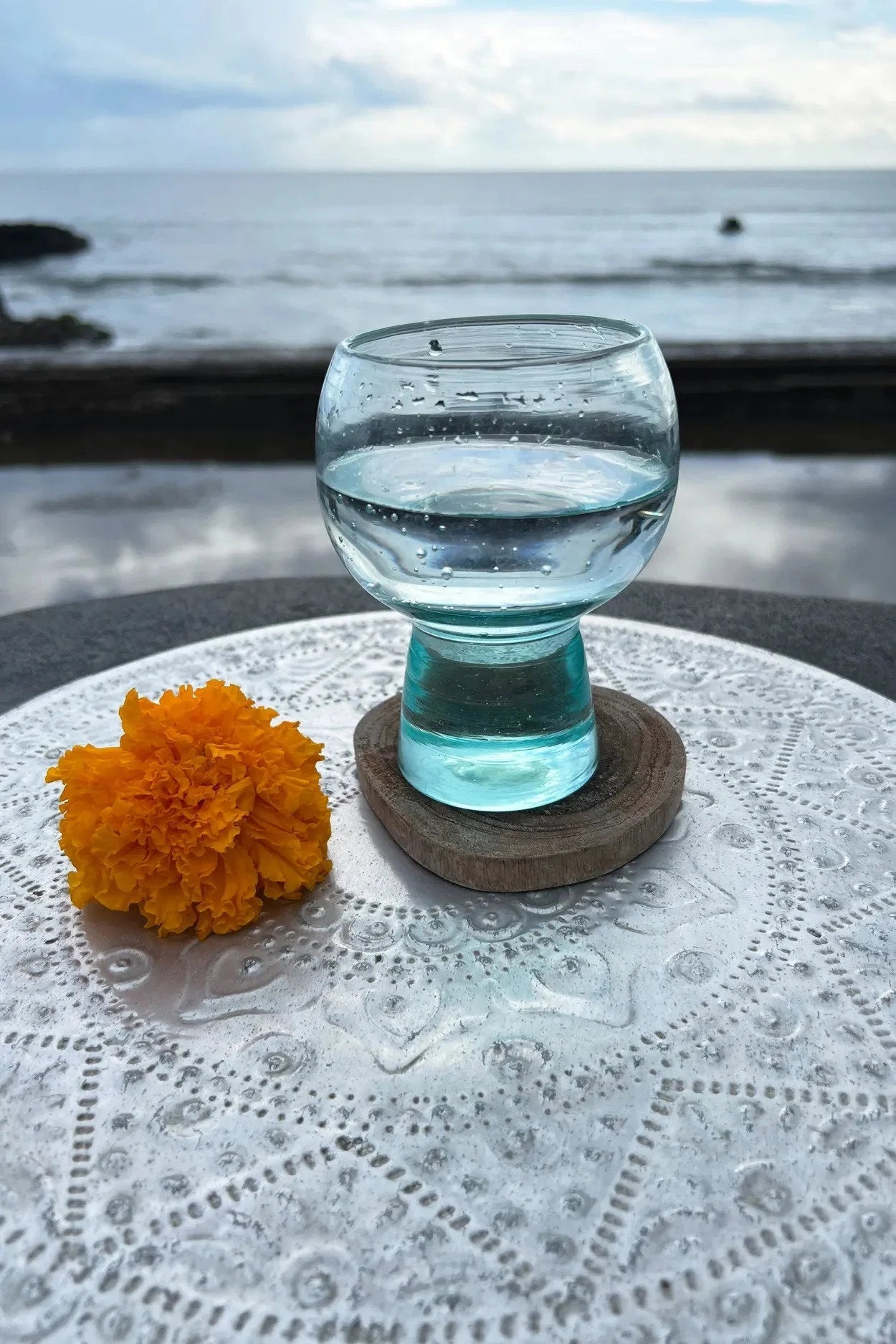 Verre à pied transparent rempli d’eau sur le dessous de verre rond en racine de teck