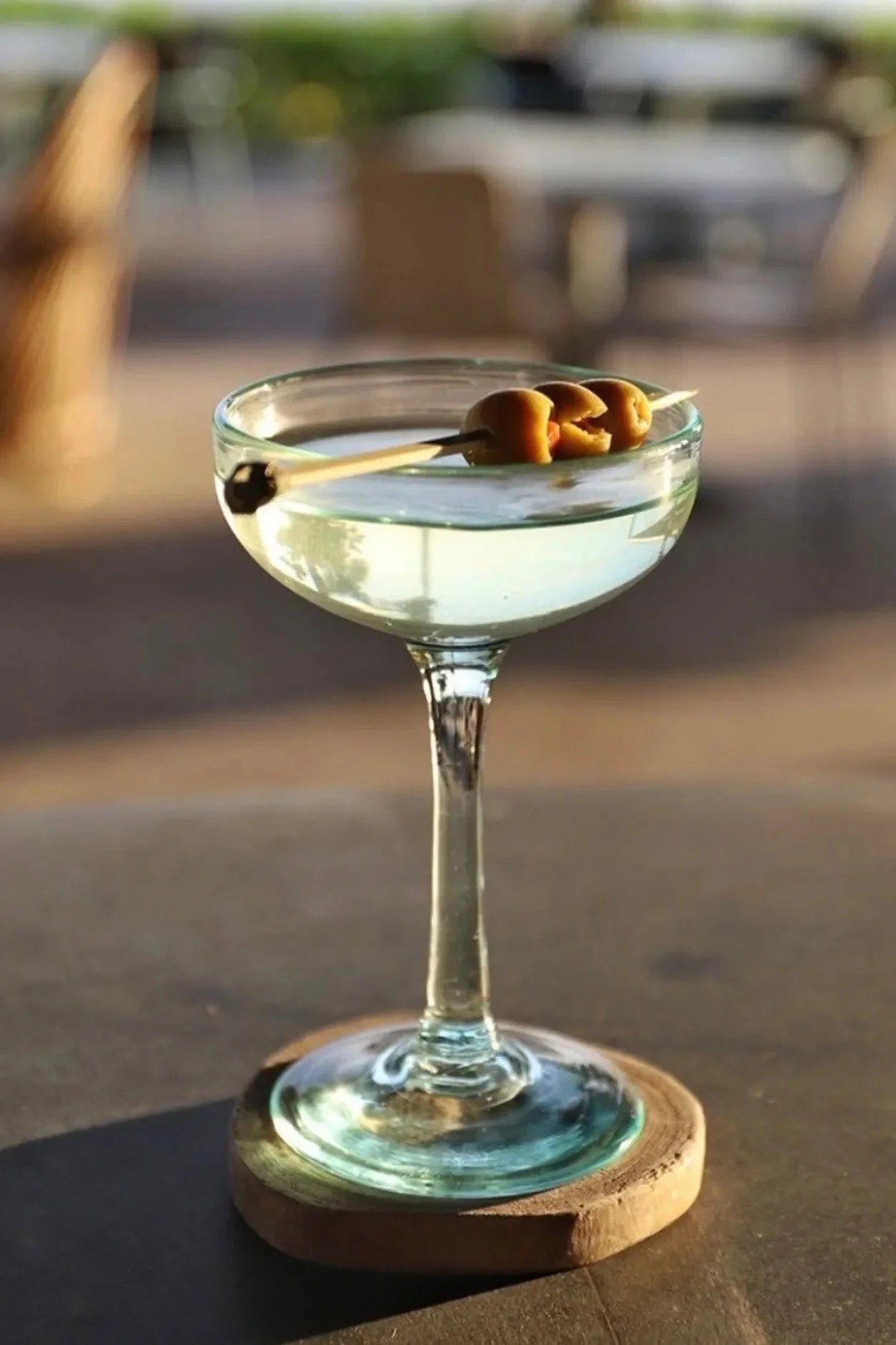 Verre à martini clair avec liquide vert pâle et trois olives sur un pique
