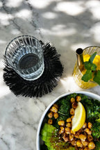 Saladier vert avec avocat, pois chiches rôtis et tranche de citron, dessous de verre rond en raphia noir avec franges