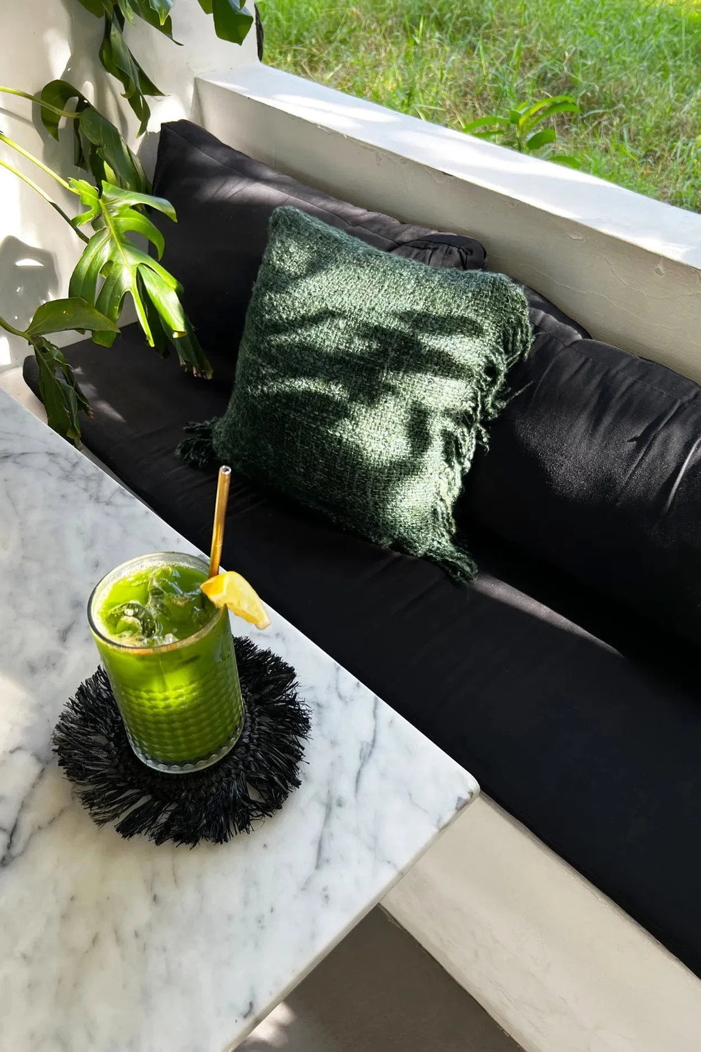 Smoothie vert dans un verre avec paille en or et tranche de citron, sur un dessous de verre rond en raphia noir avec franges