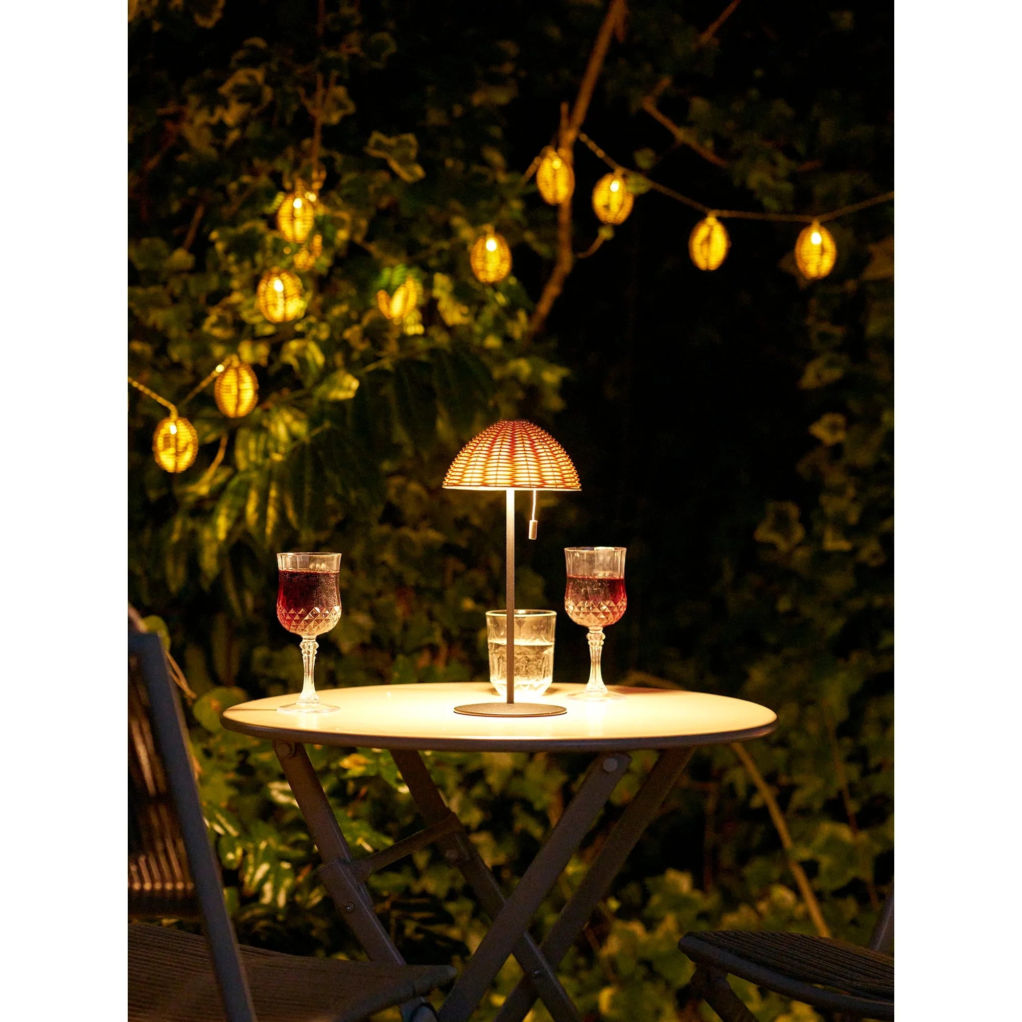 Lampe en rotin naturel ajouré sur pied métal éclairant table extérieure