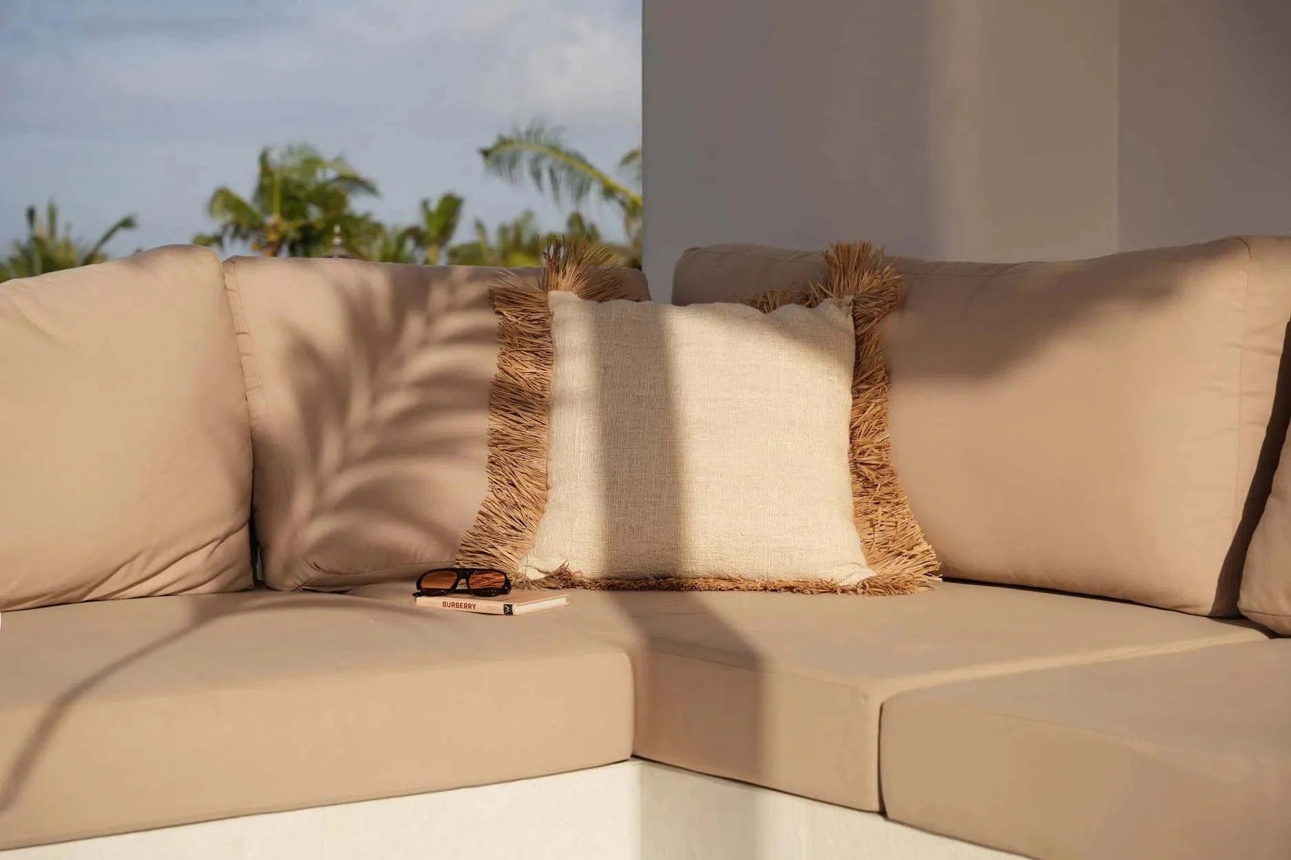 Housse de coussin carrée en coton et raphia naturel avec franges décoratives sur un canapé extérieur