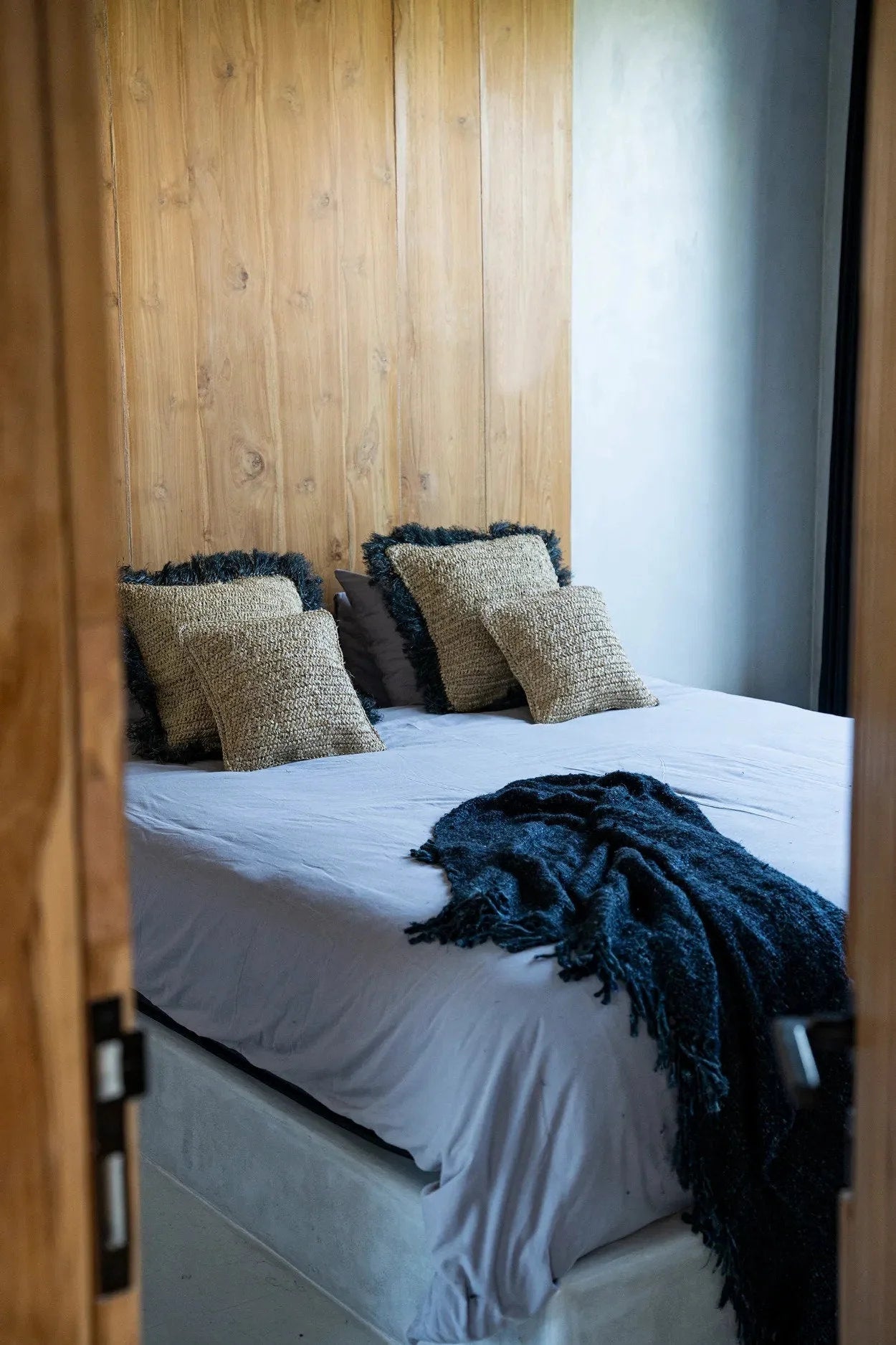 Mur en panneaux de bois avec lit blanc et couverture bleue en raphia tressé