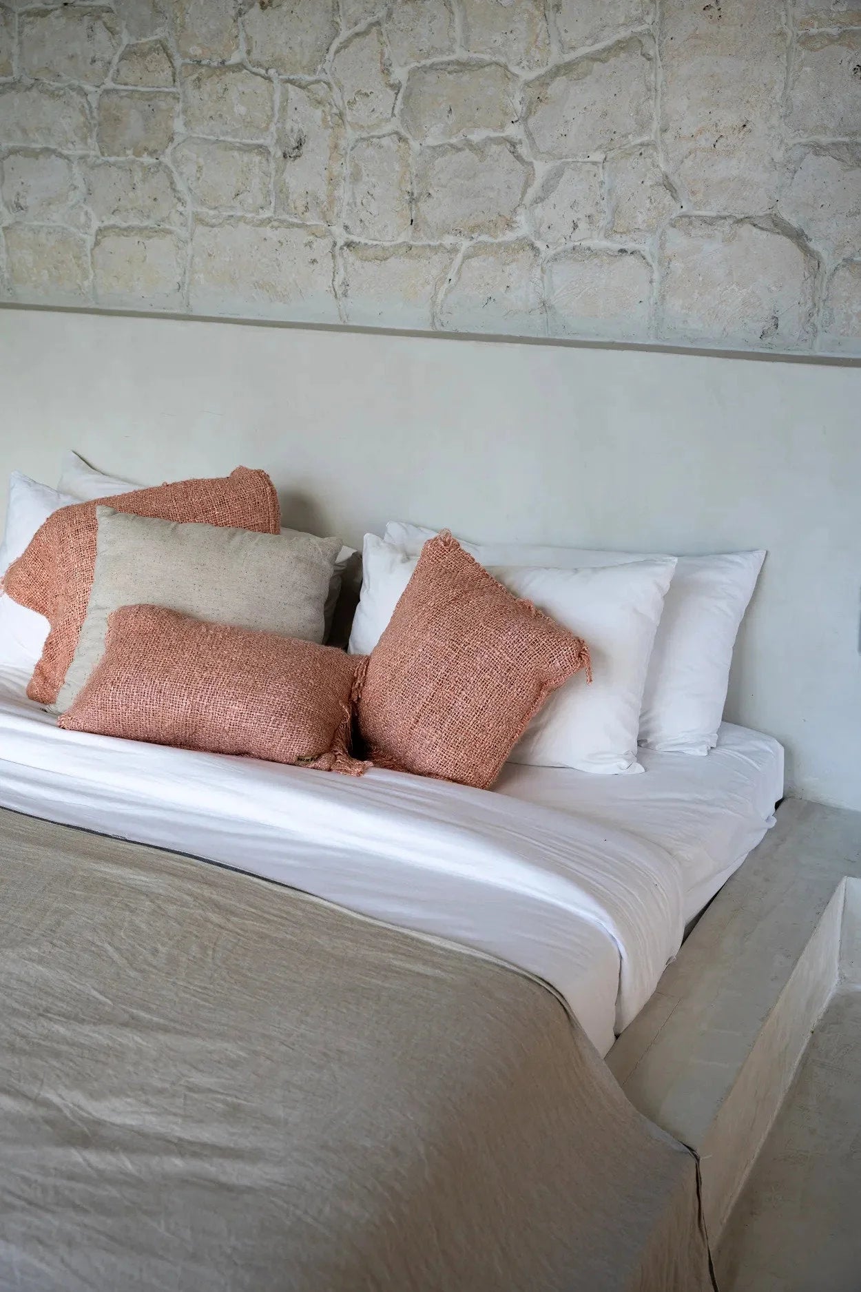 Housse de coussin en coton rose saumon 40x40 cm sur un lit avec draps blancs et coussins beige et coral