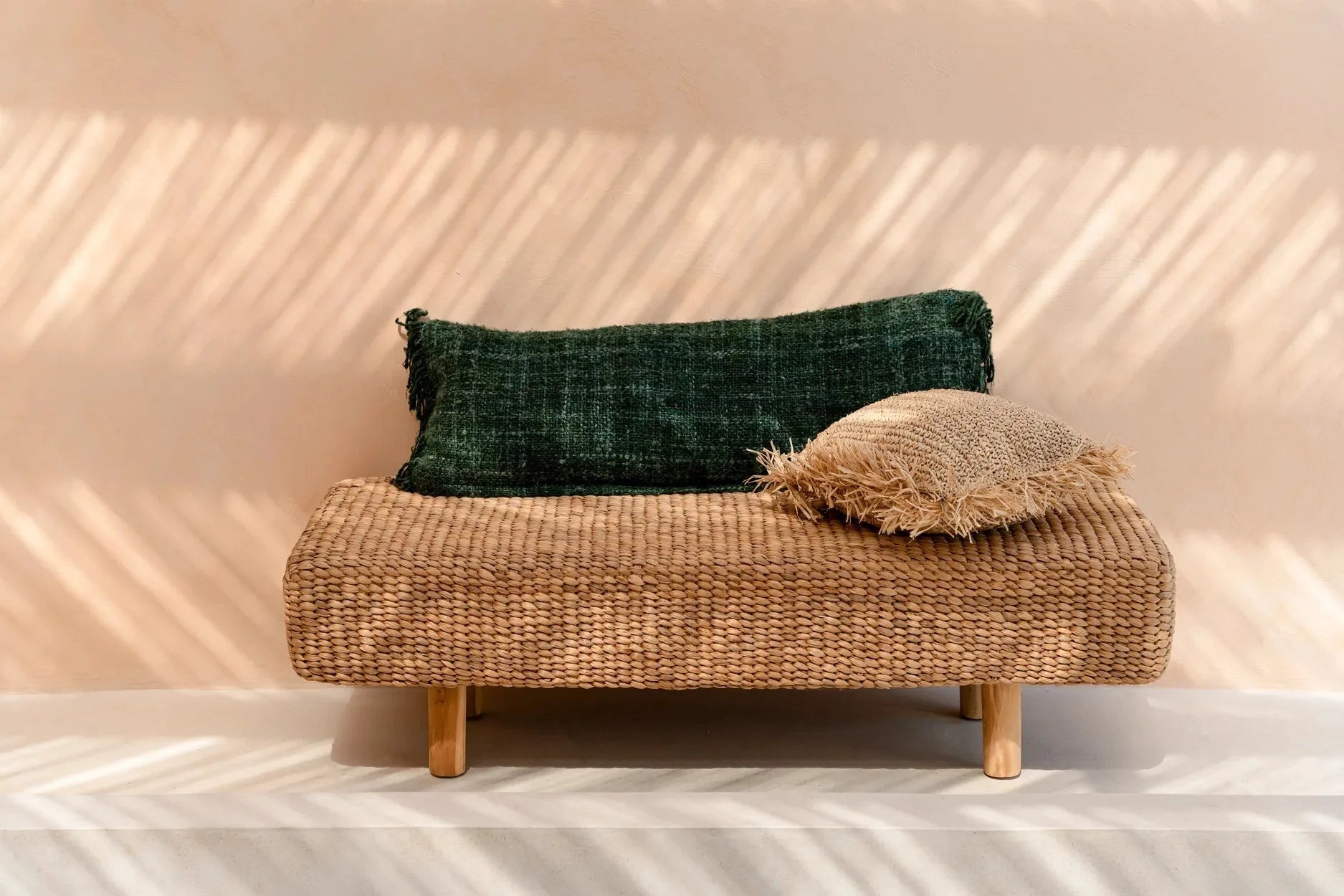 Banquette en rotin tissé avec deux coussins décoratifs verts forêt en coton
