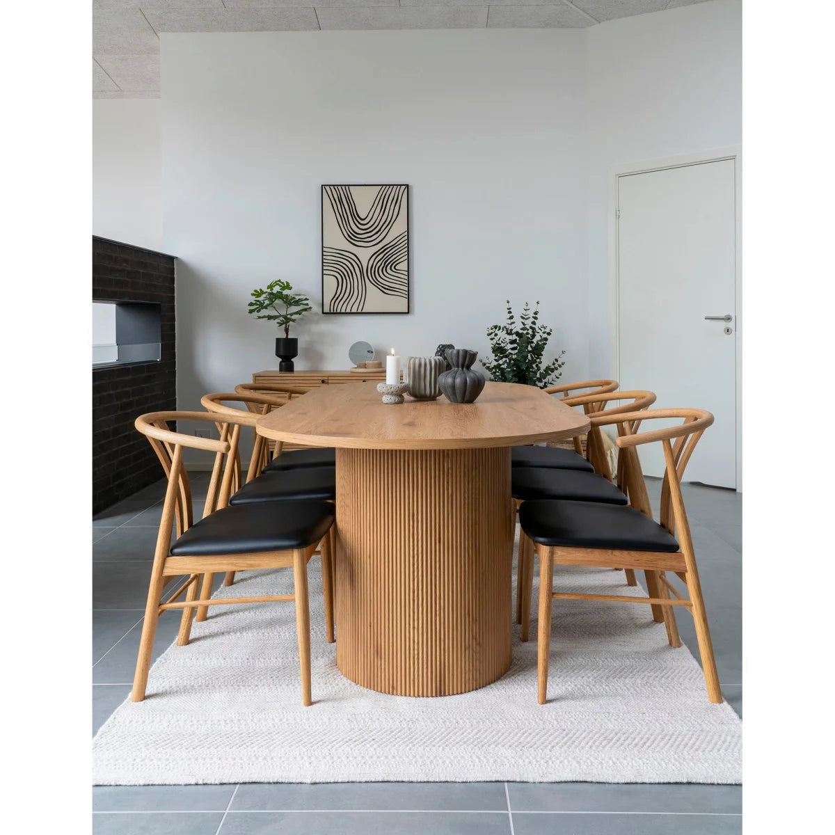 Table ovale en bois clair avec base cylindrique nervurée et chaises rembourrées cuir noir