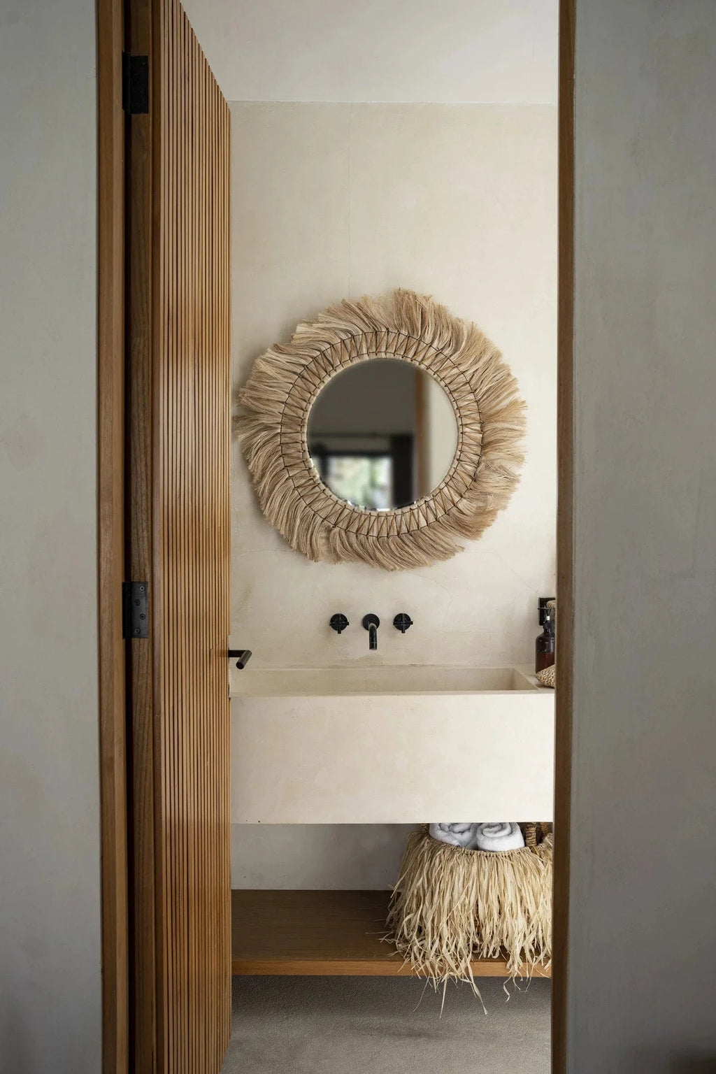 Miroir rond 90 cm en herbe naturelle tressée au-dessus d’un lavabo rectangulaire clair