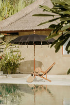 Scène de détente au bord de la piscine avec parasol balinais rond en tissu noir et sculptures en bois