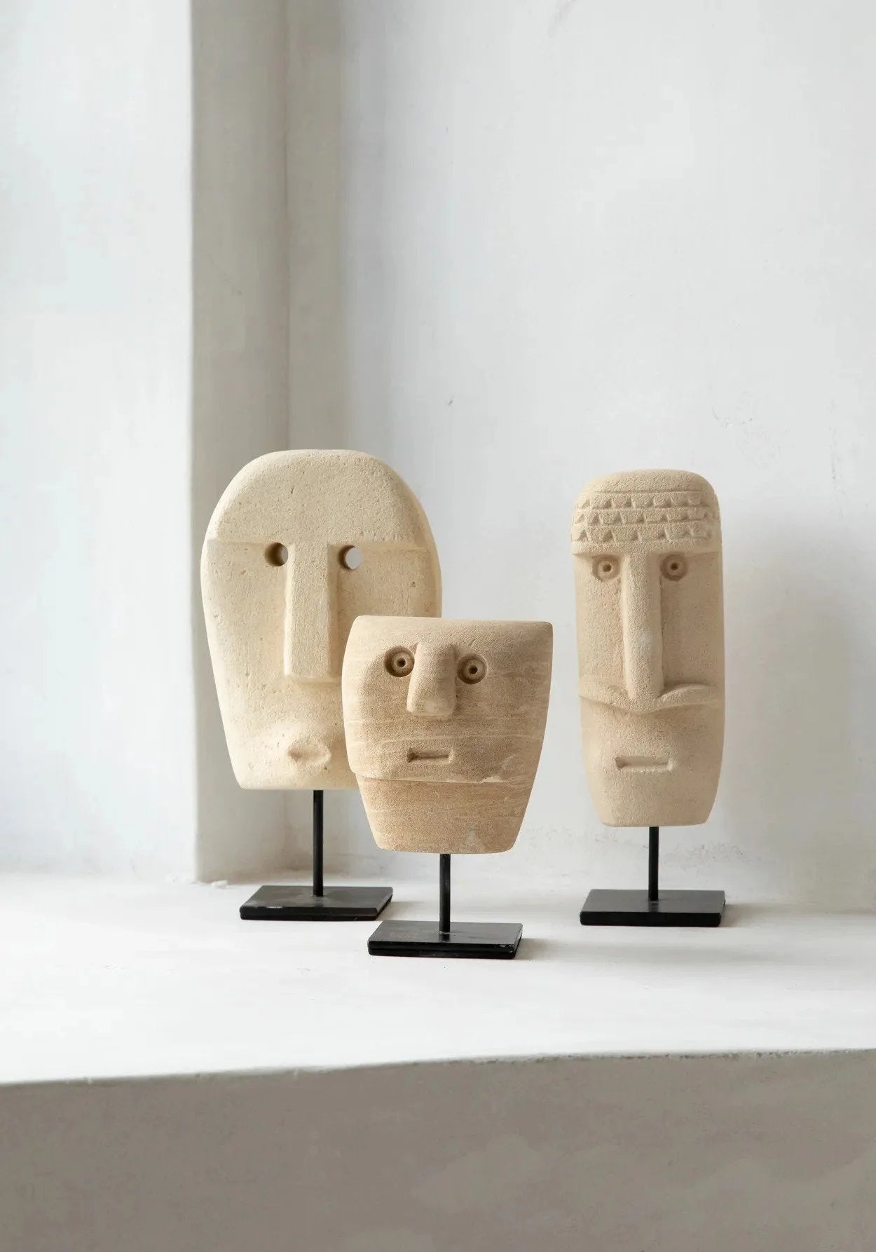 Trois sculptures en bois sculpté avec des visages abstraits sur supports en métal noir