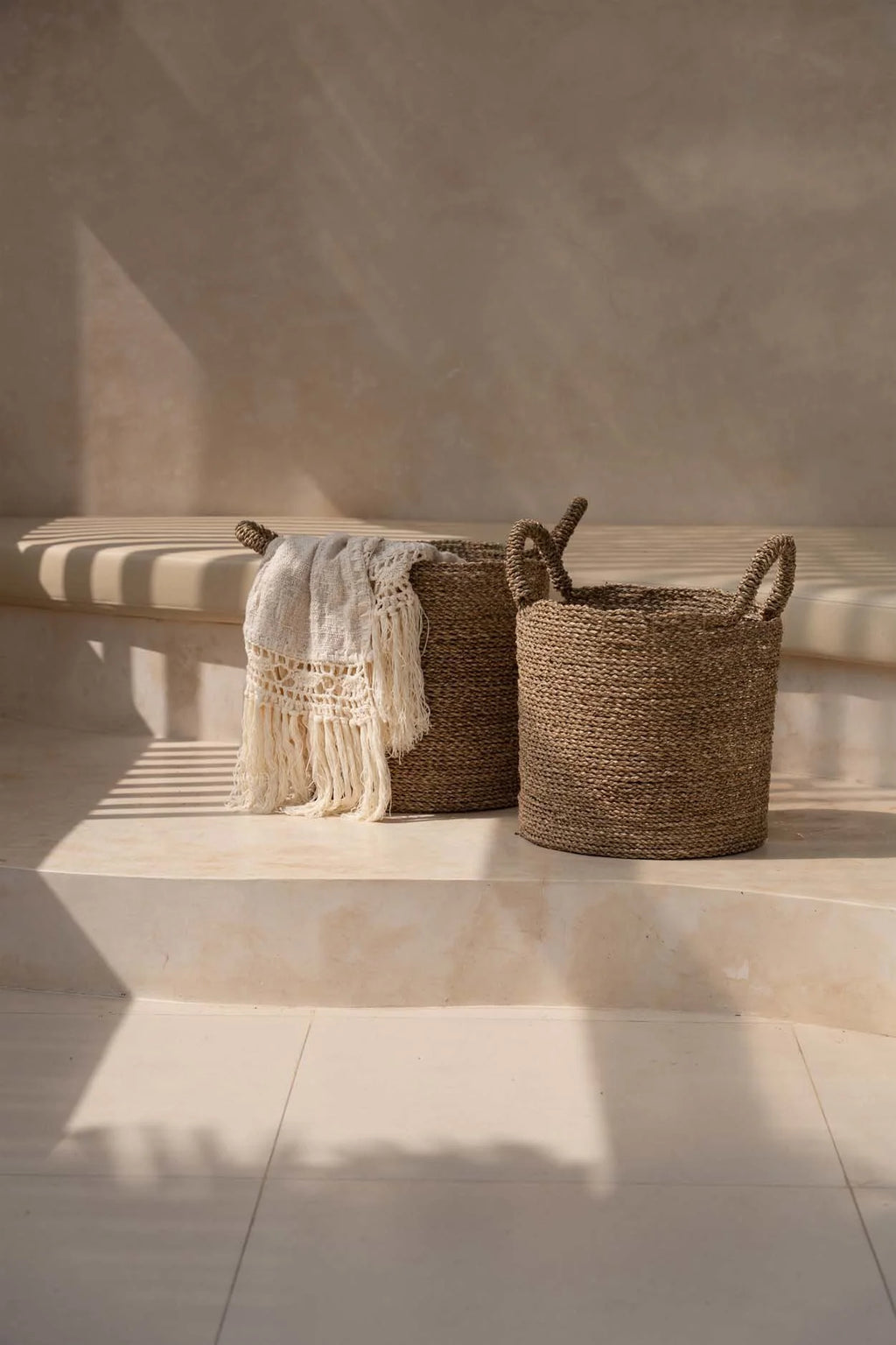 Deux paniers de rangement tissés avec couverture blanche à franges dans le plaid en coton beige bordure macramé