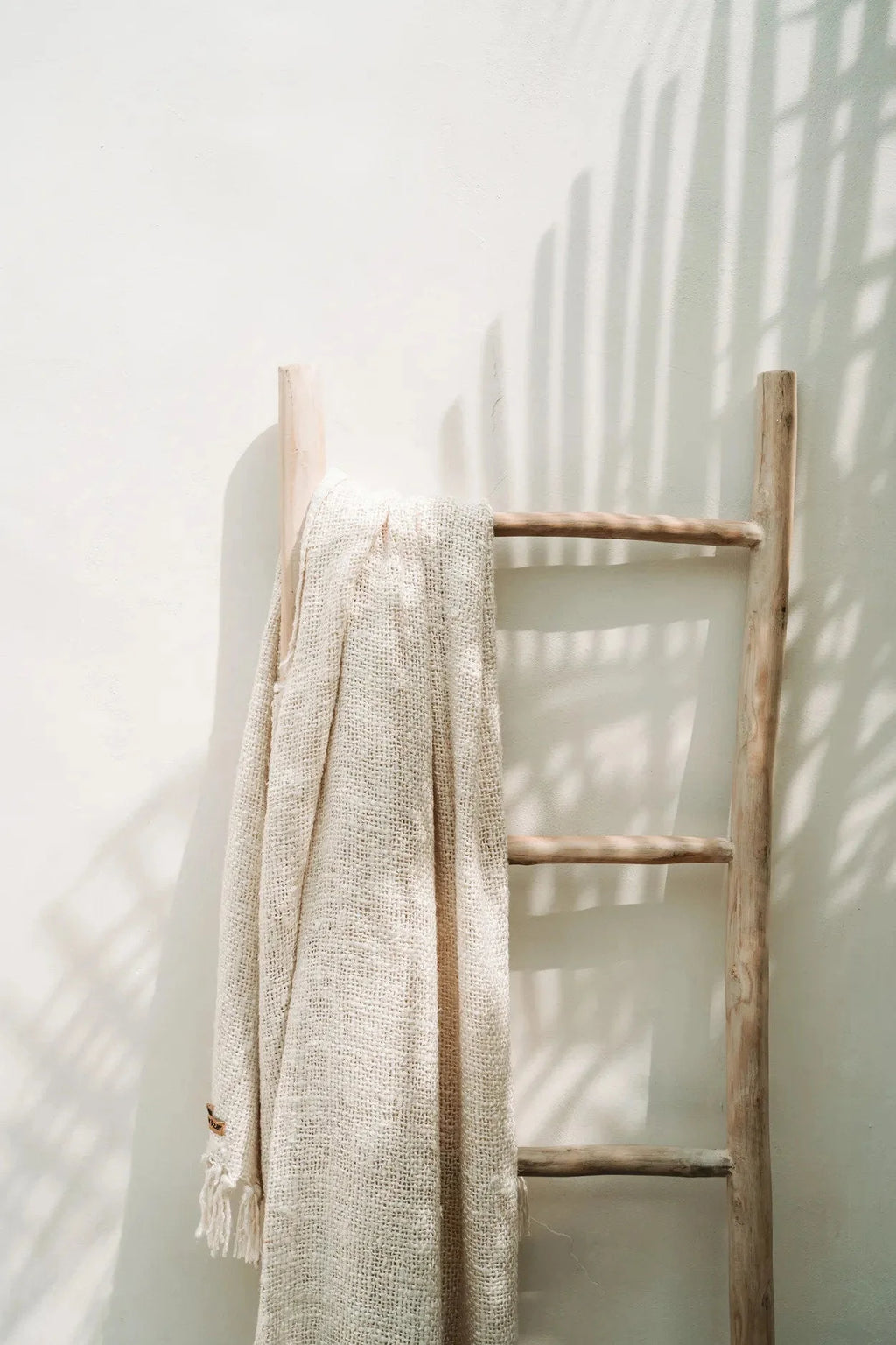 Plaid en coton gaufré crème avec franges décoratives sur une échelle en bois rustique