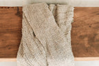 Tissu tissé beige à franges, plié sur une surface en bois, pour décoration lit ou canapé