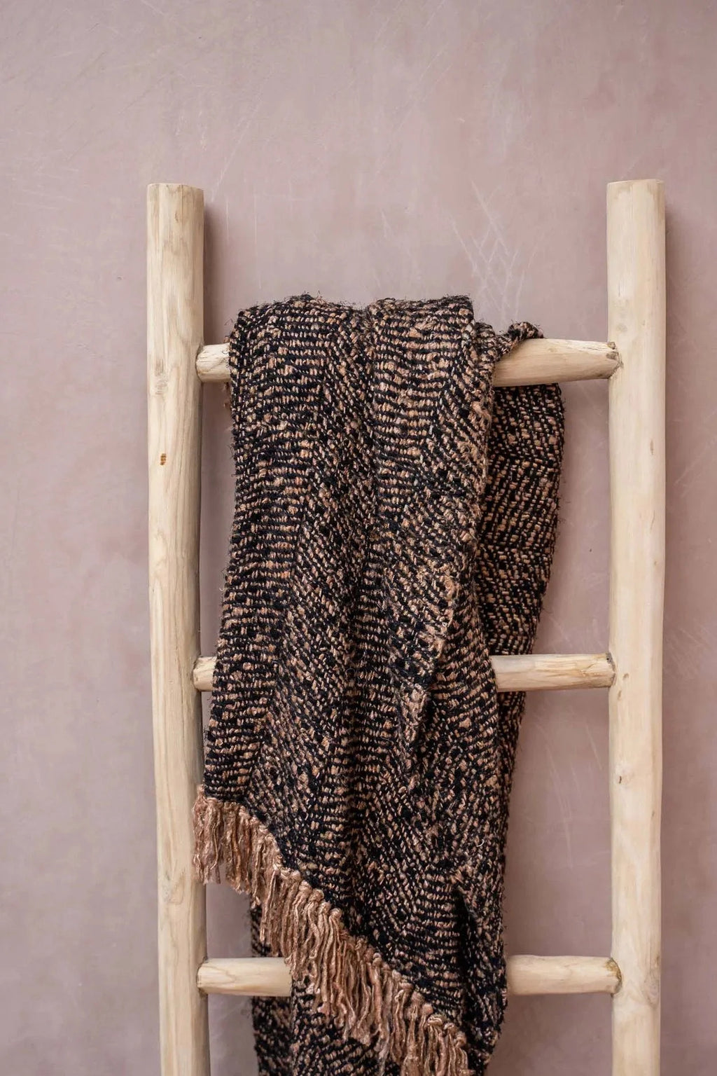 Plaid en coton tissé noir cuivre à franges chevrons sur une échelle en bois