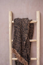 Plaid en coton tissé noir cuivre à franges chevrons sur une échelle en bois