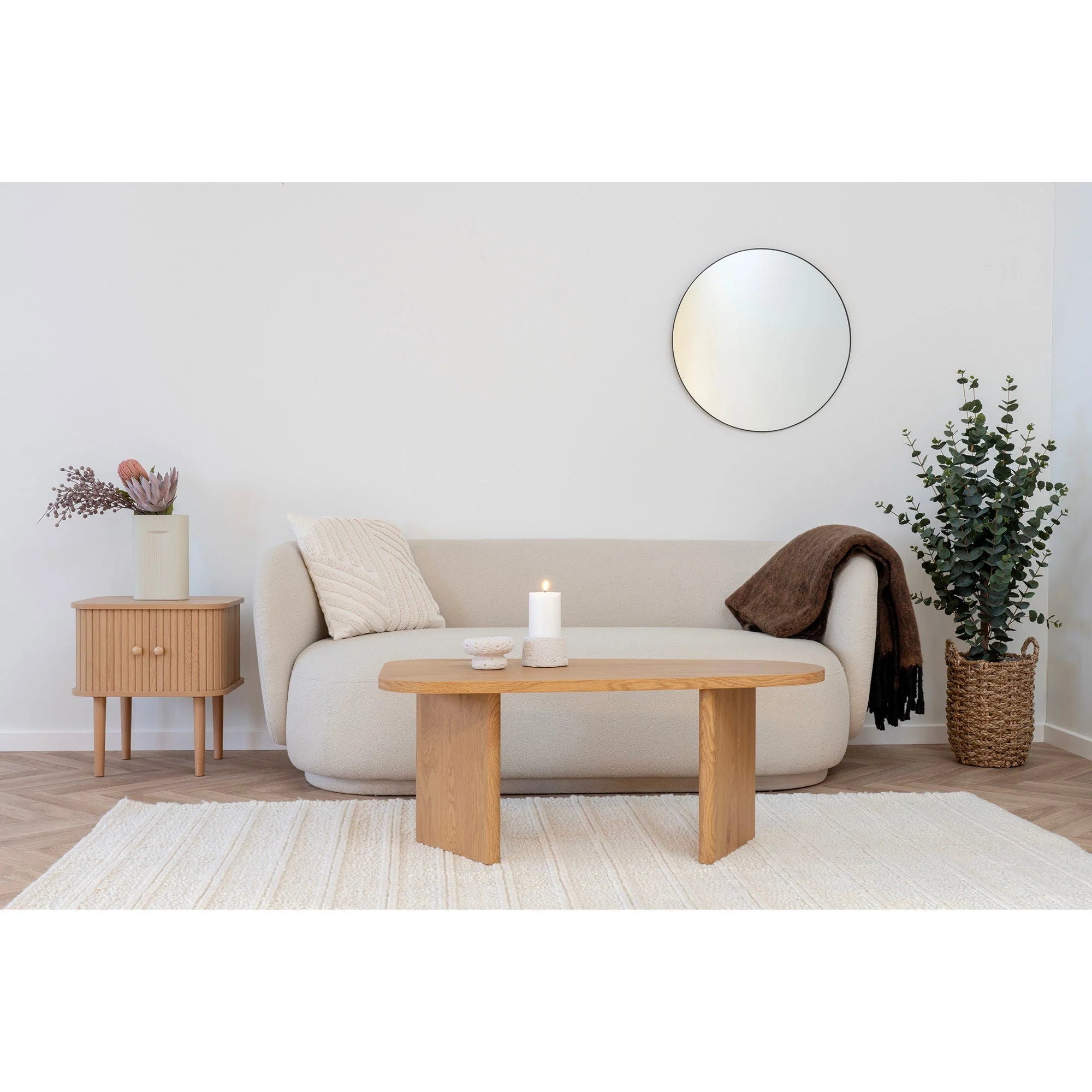Canapé beige clair capitonné avec accoudoirs ronds, coussin blanc et plaid marron à franges noires en laine mélangée