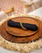 Serviette en lin noire avec anneau en perles dorées sur deux assiettes en bois rondes