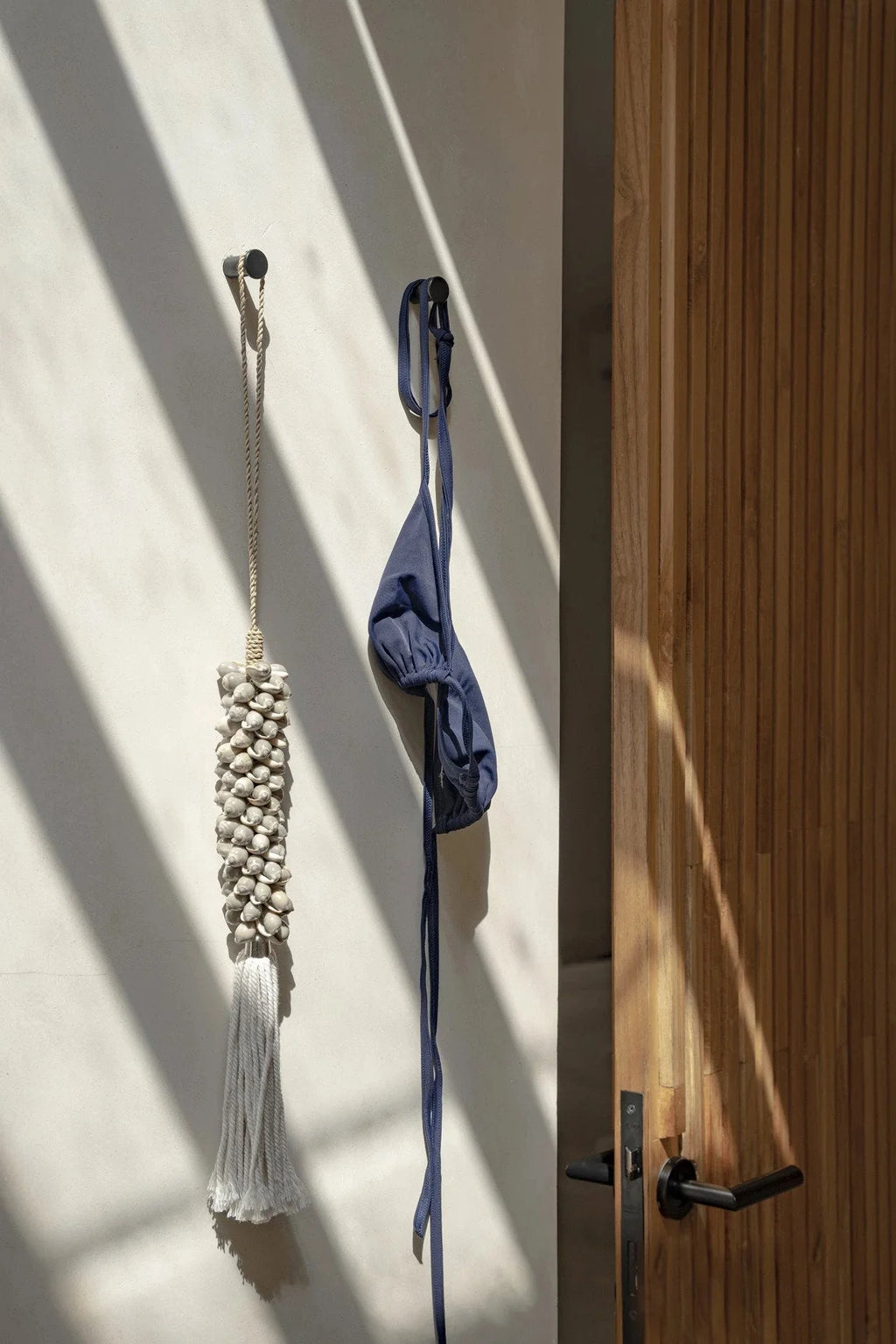 Bikini bleu suspendu sur un mur dans le mural Pompon en coquillages et coton gris perle