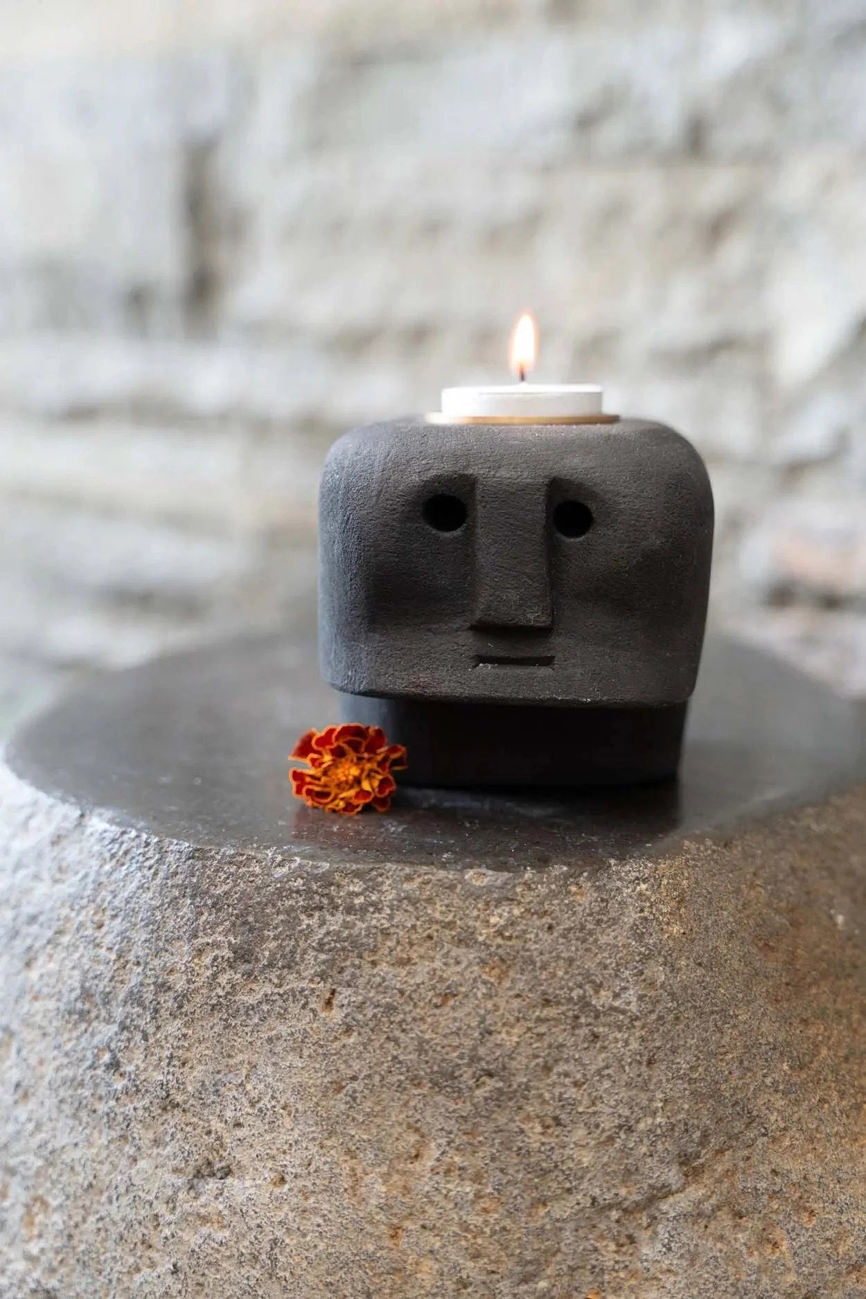 Porte-bougie en grès noir sculpté visage stylisé avec petite fleur orange à la base