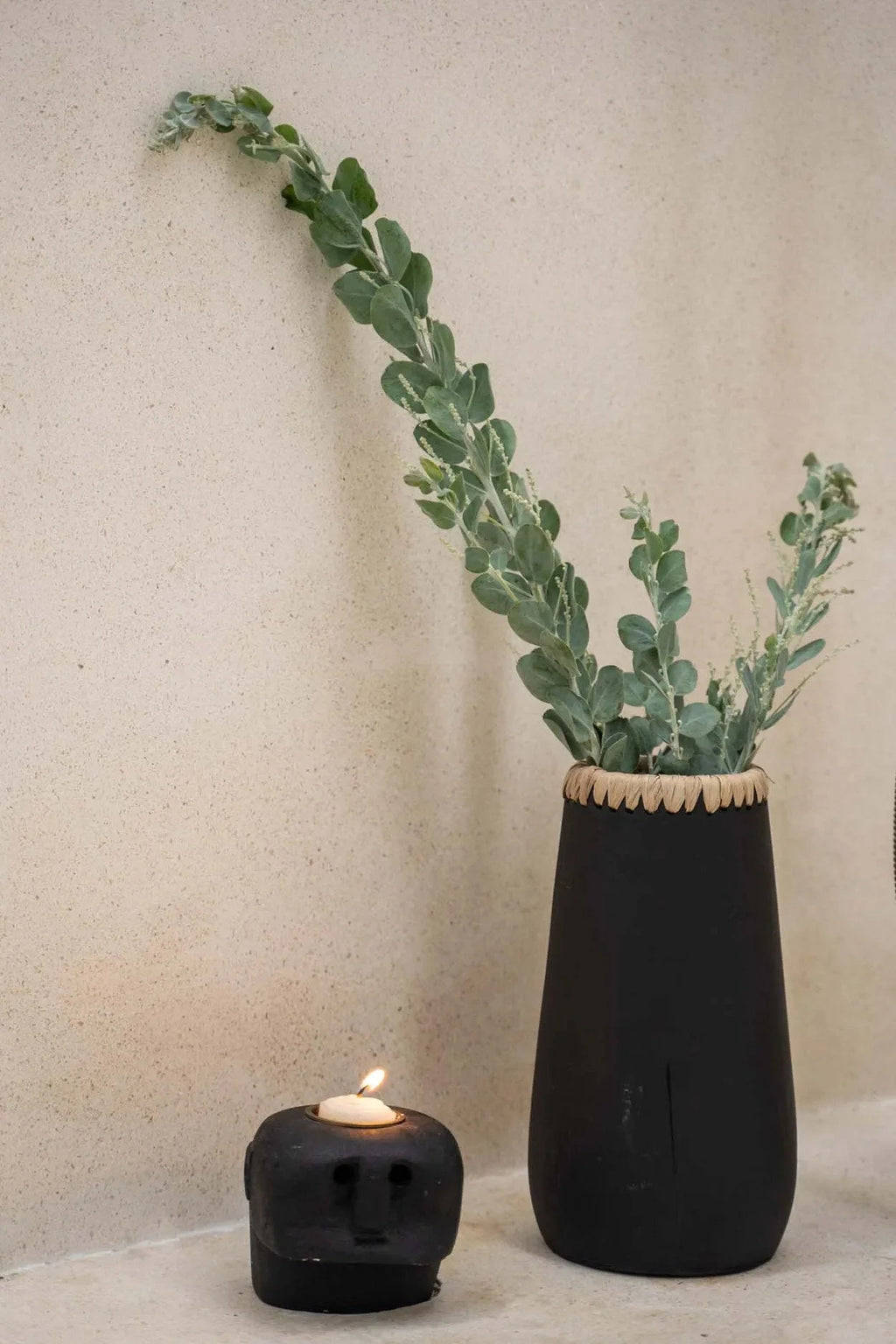 Vase noir en grès avec feuillage vert clair et bougeoir tête de mort allumé