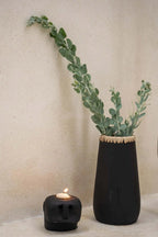 Vase noir en grès avec feuillage vert clair et bougeoir tête de mort allumé