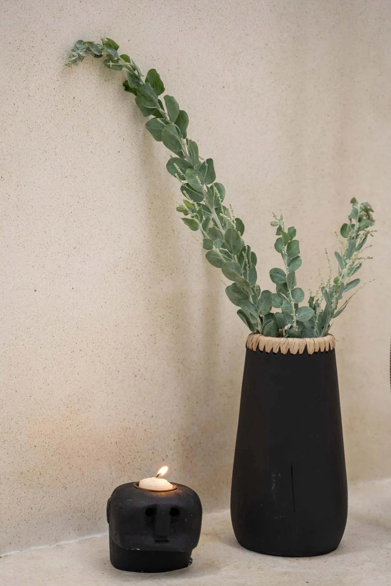 Vase noir en grès avec feuillage vert clair et bougeoir tête de mort allumé