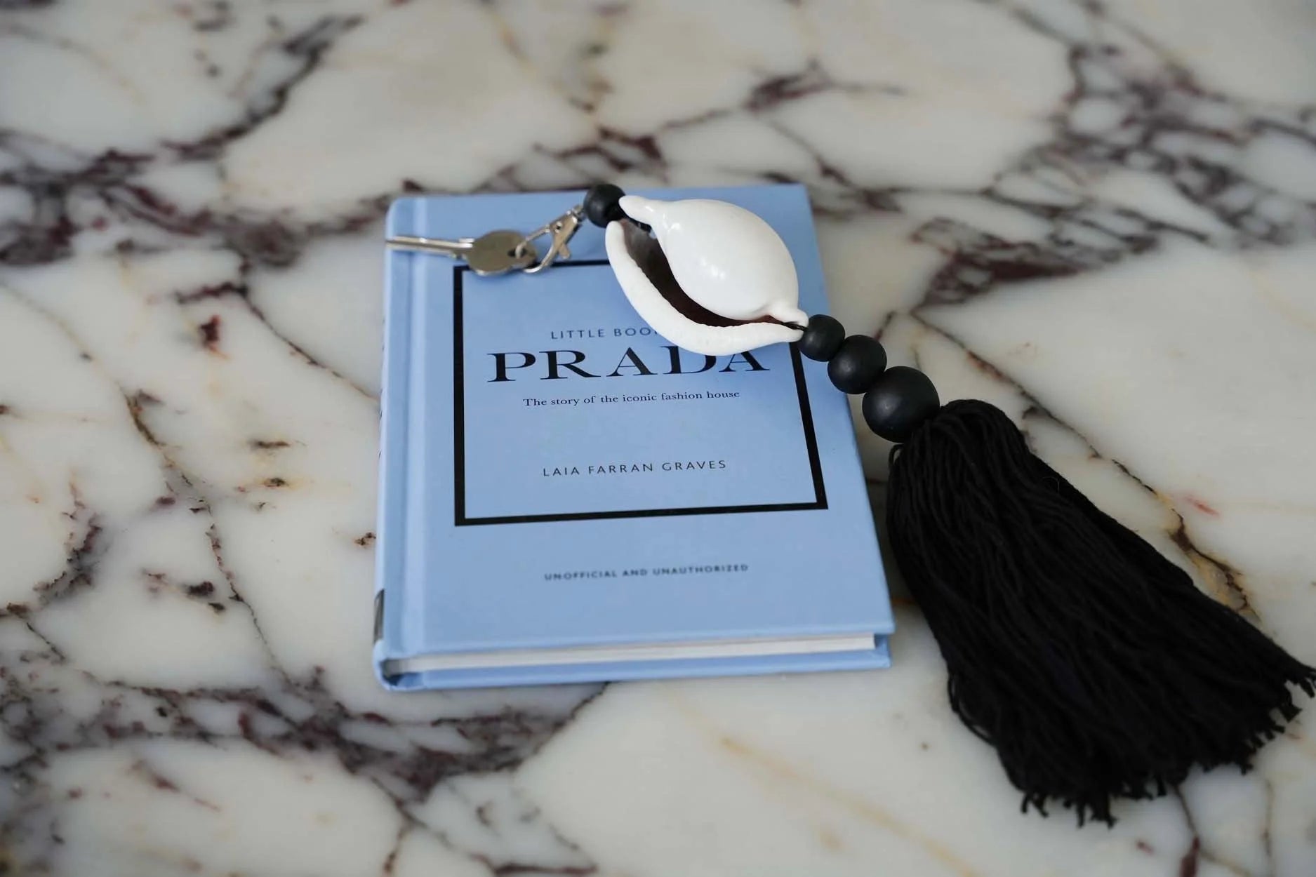 Porte-clés Prada coquillage cauri noir et blanc avec pompon en coton et cuillère blanche sur marbre