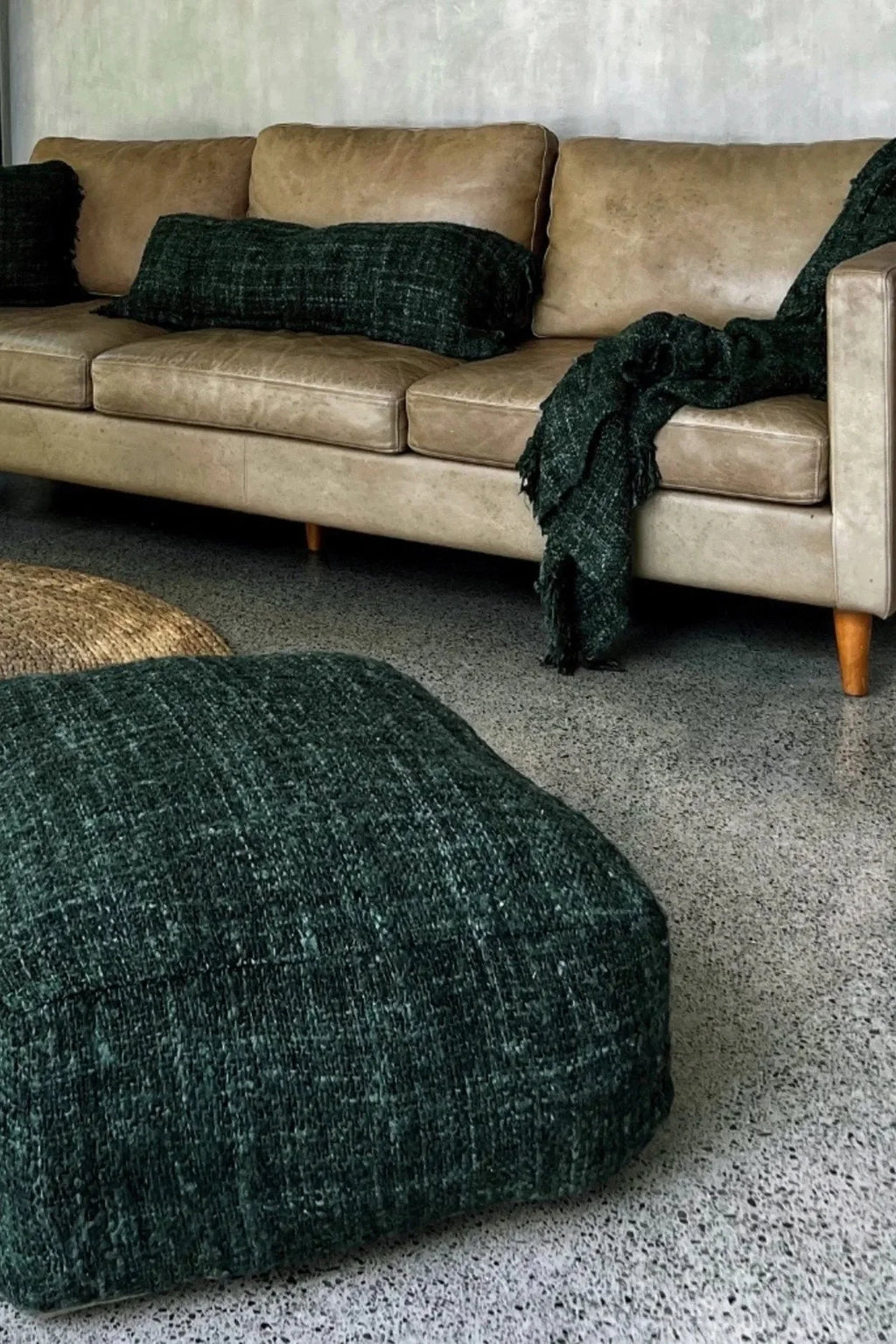 Canapé en cuir beige avec coussins verts foncés et plaid dans le salon