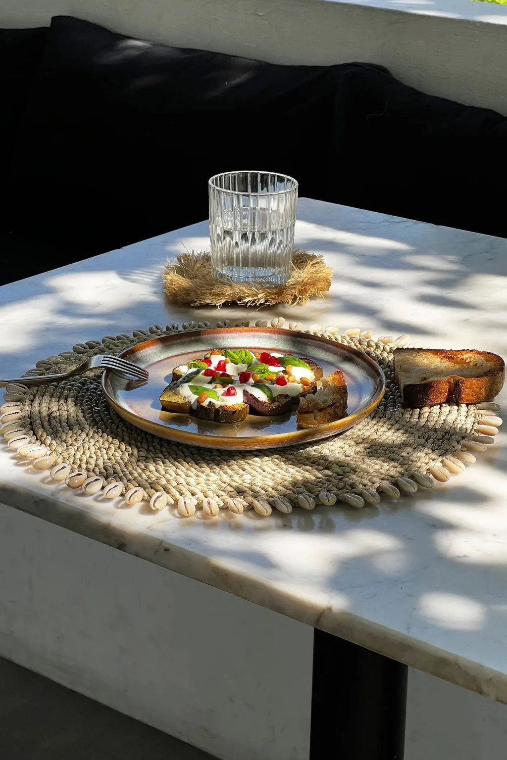 Assiette de toast à l avocat avec graines de grenade et verre d eau sur un set de table rond en jonc de mer avec coquillages naturels