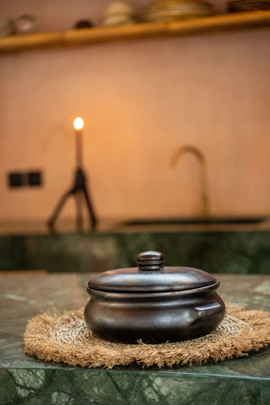 Pot en terre cuite noire avec couvercle sur un tapis tissé, parfait pour la table