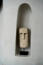 Sculpture visage en grès beige texturé avec nez et yeux profonds sur socle en bois