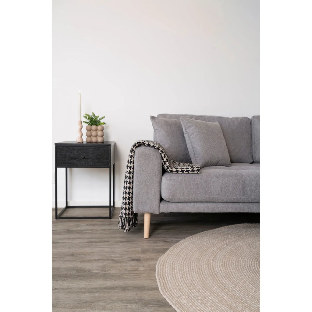 Canapé gris capitonné avec pieds en bois et plaid houndstooth sur laccoudoir