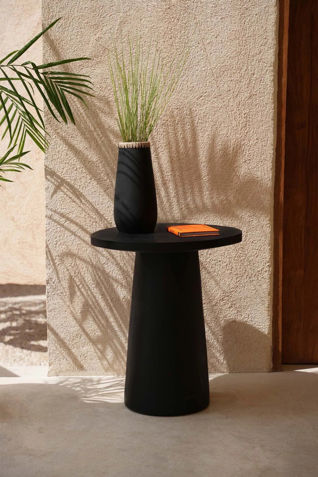 Table d’appoint conique en bois de Munggur noir avec vase de tall grass et livre orange