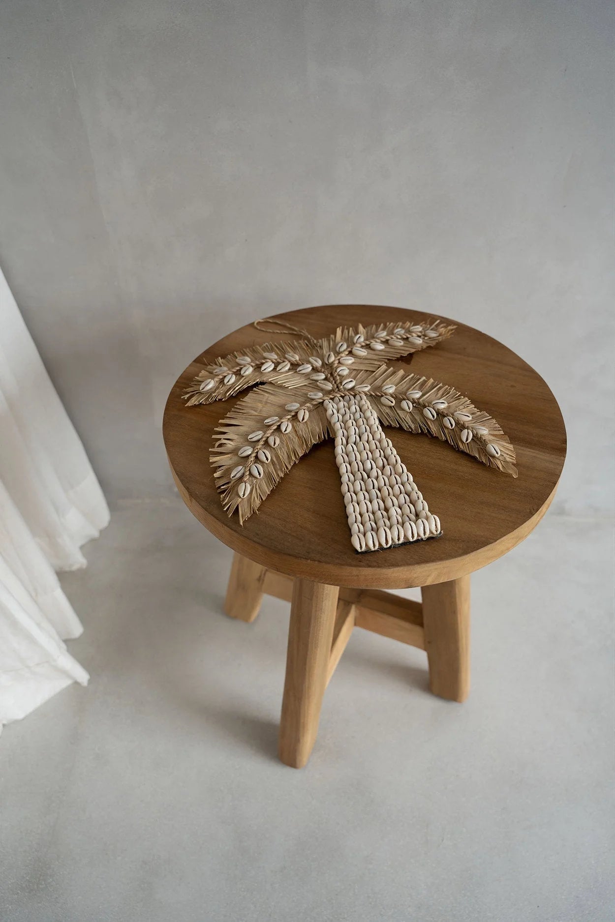 Ornement artisanal de palmier en coquillages beiges et paille tressée sur tabouret rond en teck massif Ø35 cm