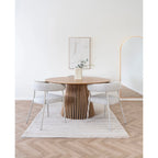 Table ronde en bois avec base cannelée et deux chaises tapissées, près d’un tapis rectangulaire fait main en laine ivoire à rayures 160x230 cm