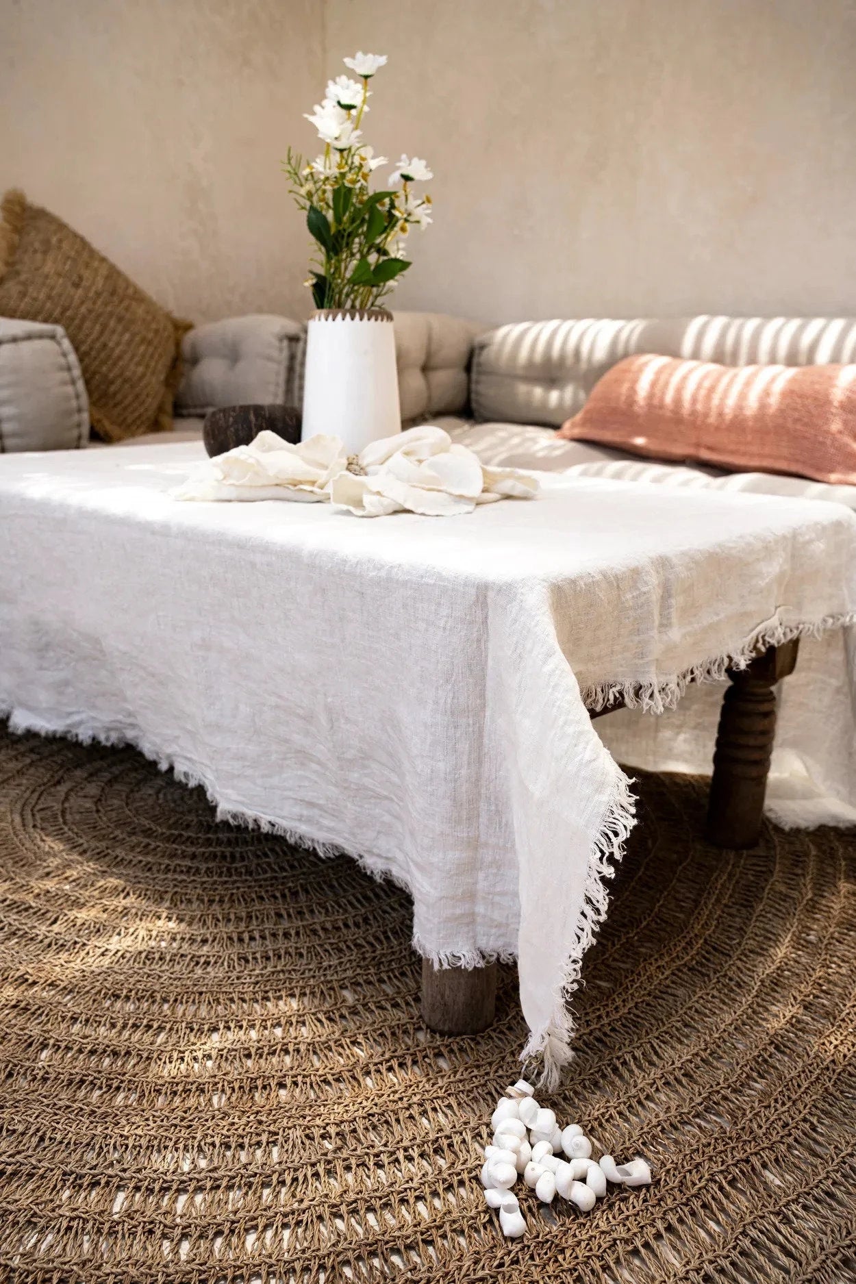 Table en jonc de mer naturel avec un tapis rond en style bohème et une nappe en lin blanc à bords effilochés
