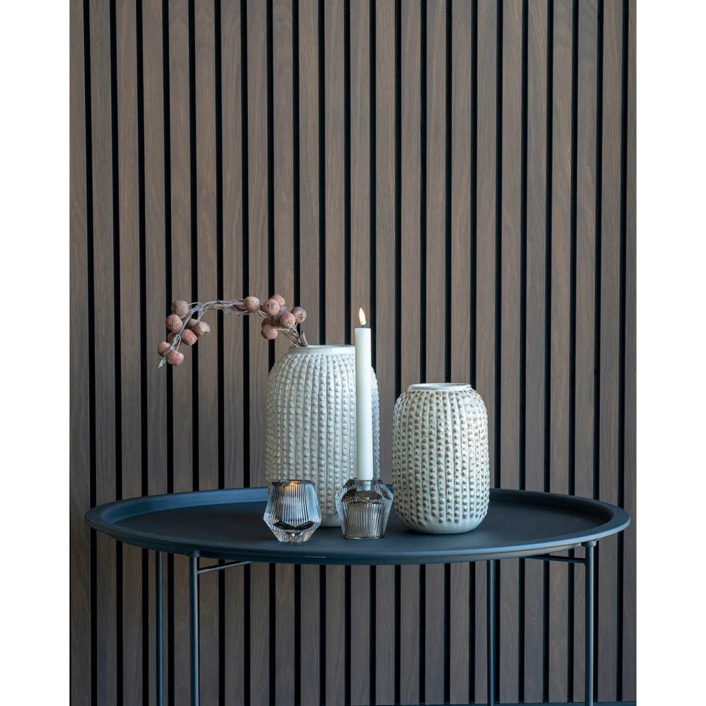 Deux vases céramique texturés écru à col étroit, l’un avec baies séchées, l’autre près d’une bougie allumée sur table sombre